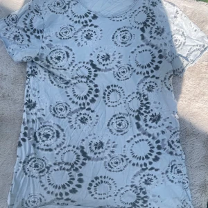 Tie-dye t-shirt i grått och vitt XL - Säljer en  t-shirt i storlek XL.  T-shirten är vit med grått tie-dye mönster i cirklar och har korta ärmar. Materialet känns mjukt och svalt, perfekt för en chill och avslappnad stil.