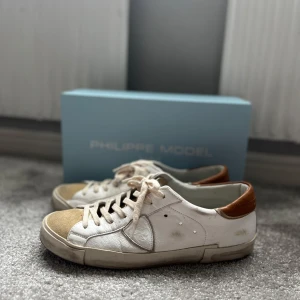Vita sneakers från Philippe Model - Snygga vita sneakers från Philippe Model med bruna detaljer. Skorna har klassisk snörning och en stilren design. Perfekta för en avslappnad och trendig look. Använda ett fåtal gånger. Pris kan diskuteras. Ny pris 3250.