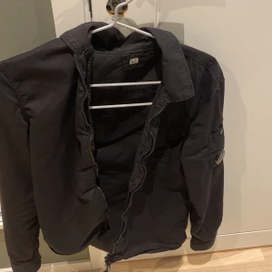 C.P. Company overshirt  - C.P company i klassisk svart, 100 % äkta. För att bevisa äktheten finns en QR-kod på en av bilderna. QR-koden är dock täckt i annonsen för att forhindra att den blir ogiltig om flera skannar den. Skicka ett meddelande om du är intresserad, så skickar jag koden direkt till dig! Detaljer: • Marke: C.P Company • Färg: svart • Storlek:S • Skick: 10/10 • Material: Bekvamt och slitstarkt tyg Tröjans ikoniska C.P Company -logo bricka  på vänster ärm gör den igenkännbar och ger en exklusiv touch. 
