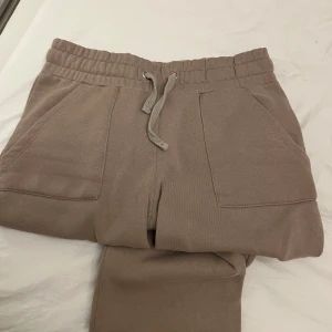 Beige mjukisbyxor med snörning S - Beiga mjukisbyxor i mjukt bomullsmaterial med bred resår och snörning i midjan. Byxorna har raka ben, två stora fickor fram och två bakfickor. Perfekta för chill dagar eller när du vill vara extra bekväm.