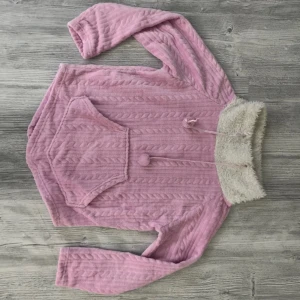 Ljusrosa myströja från Damella Small/medium - Supermjuk ljusrosa tröja från Damella med kabelstickat mönster, stor magficka och fluffig vit krage. Tröjan har långa ärmar, dragsko med bollar, en är påväg att lossna. Perfekt när du vill mysa till max. Passar storlek 36/38