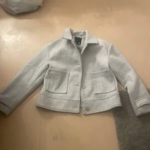 Ljusgrå kavajjacka från 157, M - Snygg ljusgrå kavajjacka från 157 med klassisk krage, stora fickor framtill och knäppning med knappar. Jackan har en rak och lite boxig passform, perfekt för dig som gillar stilren och enkel design. Materialet känns mjukt och passar bra till både jeans och kostymbyxor.