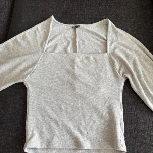 Ljusgrå långärmad topp med fyrkantig ringning - Superfin ljusgrå långärmad topp med fyrkantig ringning och lite croppad passform. Mjuk och stretchig i bomullsmix, perfekt till jeans eller kjol. Enkel och stilren design som funkar året runt.
