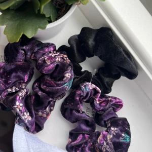 3-pack scrunchies - Säljer ett 3-pack scrunchies från Beauty Care. Två av dem är lila med blommigt mönster och en är helsvart. Alla är i glansigt satinliknande material som känns lyxigt och mjukt mot håret. Perfekta för att piffa till din frisyr.
