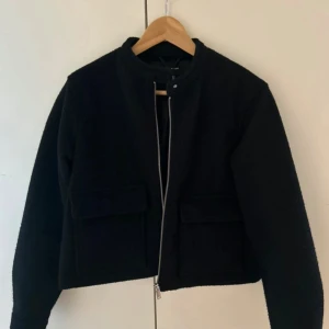 Svart ulljacka från Vero Moda XS - Snygg svart jacka från Vero Moda i ullblandning. Modellen är croppad med raka linjer, två stora fickor framtill och dragkedja. Perfekt för dig som gillar minimalistisk stil och vill ha en jacka som funkar till många outfits.