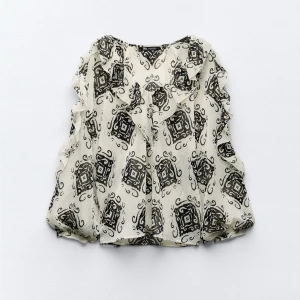 Mönstrad volangblus i chiffong - Supersöt blus i tunn, luftig chiffong med svart och vit grafiskt mönster. Volangdetaljer längs axlarna ger en extra touch. Perfekt för dig som gillar unika prints och en lätt, flowy känsla.