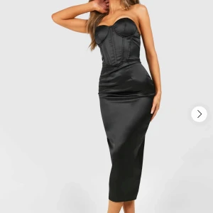 Svart axelbandslös satinklänning - Supersnygg svart långklänning i satin med axelbandslös design och markerad byst. Jättefin klänning men har aldrig använt den, etiketten finns på kvar. Köpt för jätte länge sen för 650kr. 