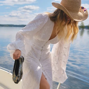 Vit långklänning med puffärmar - Superfin vit långklänning från adoore med v-ringning, markerad midja och knappar framtill. Klänningen har puffiga långärmar och broderade blommor i tyget. Snygg slits framtill och romantisk känsla, perfekt för sommarens alla tillfällen. Klänningen är använd 2-3 gånger och är inte sönder någonstans har ni förslag på pris så är det bara att skriva 🫶🏻😊 storlek 38❤️