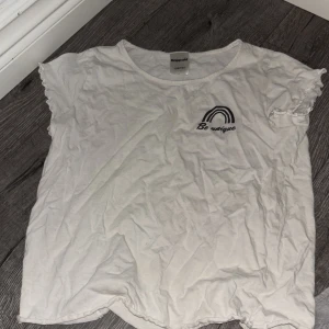 Vit t-shirt med tryck från Kappahl - Vit t-shirt från Kappahl med svart tryck av en regnbåge och texten 'Be unique' på bröstet. T-shirten har korta ärmar med lätt volangkant och är gjord i mjuk bomull. Perfekt och sova i