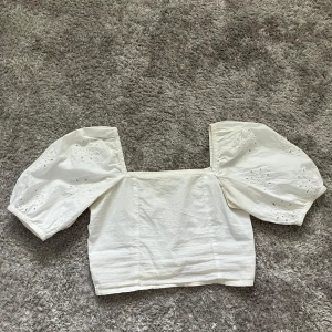 Vit croppad blus med puffärmar - Superfin vit croppad blus med fyrkantig ringning och stora puffärmar med broderade detaljer. Toppen har smockad rygg för extra komfort och är perfekt för en somrig look. Tillverkad i bomull och har en luftig känsla.