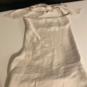 Champagnefärgad halterneckklänning - Supersnygg champagnefärgad halterneckblus i glansigt satinliknande material. Blusen har öppen rygg och knyts med breda band i nacken för en chic look. Använd fåtals gånger säljer då den ej kommer till användning 