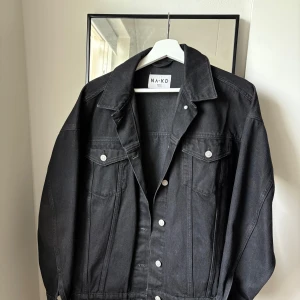 Svart jeansjacka från NA-KD, strl 34 - Snygg svart jeansjacka från NA-KD i klassisk modell med silverfärgade knappar och två bröstfickor. Jackan har en rak passform.