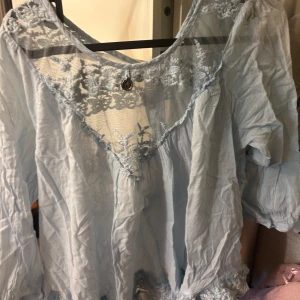 Ljusblå blus med spetsdetaljer - Jätte söt ljusblå blus med v-ringning och spets upptill. Blusen har trekvartsärmar och volangkant med spets nertill. Perfekt topp för sommaren!💞