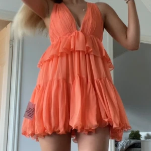Korallfärgad volangklänning  - Superfin kort volangklänning i korall med djup v-ringning och omlottband i ryggen❤️helt ny perfekt till midsommar