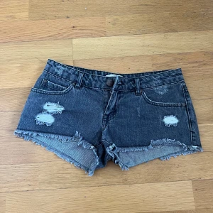 Mörkgrå jeansshorts - Mörkgrå lågmidjade jeansshorts från Pull&Bear med slitna detaljer och fransig kant. I stl 36 men skulle säga att de är små i storleken så passformen motsvarar stl 34.