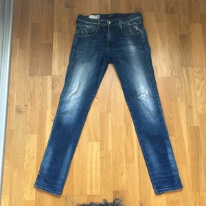 Blå Replay jeans med snygga detaljer W30 L32 - Blå jeans från Replay med snygga slitningar och kontrastsömmar. Klassisk femficksmodell med raka ben och coola bakfickor med broderade detaljer. Perfekta för dig som gillar en avslappnad men ändå stilren look.