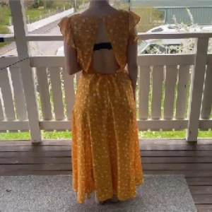Gul blommig mesh långklänning med slits - Superfin gul mesh långklänning med vita blommor, v-ringning och volangärmar. Klänningen har öppen rygg och en snygg slits framtill. Perfekt för sommarens alla tillfällen och ger en riktigt härlig vibe.