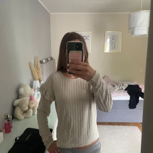 Beige ribbad tröja med volangärm Lindex - Säljer en beige ribbad tröja från Lindex i storlek 170. Tröjan har långa ärmar med volangdetalj på axlarna och rund halsringning. Perfekt för dig som gillar en enkel men ändå söt stil.