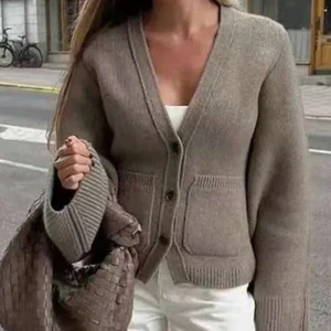 Beige stickad kofta med knappar - Snygg beige stickad kofta med v-ringning och stora knappar framtill. Koftan har två fickor och långa ärmar med breda muddar. Perfekt att slänga över en topp för en chill och stilren look.