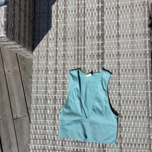 Turkos ribbad linnetopp Urban Outfitters - Säljer en turkos ribbad linnetopp från Urban Outfitters. Toppen är ärmlös med djup v-ringning och croppad passform, perfekt för varma dagar. Mjuk och stretchig i bomullsmix, 