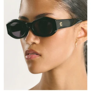 Svarta solglasögon från Corlin - Snygga svarta solglasögon från Corlin med ovala, kantiga bågar och mörka linser. Tjocka skalmar med guldfärgad logga på sidorna ger en cool och modern vibe. Perfekta för att lyfta vilken outfit som helst. Köpta för 1 299kr och säljs för 1099kr, aldrig andvända. Man får med fodral till solglasögonen! 