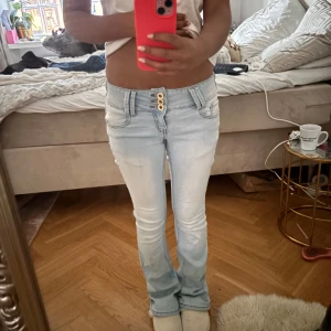 Ljusblå bootcut jeans Girl VIVI - Säljer ett par ljusblå jeans från Girl VIVI med tre snygga knappar i midjan. Jeansen har bootcut-modell, klassiska fickor fram och bak samt bälteshällor. Perfekta för dig som gillar en retro vibe och vill ha ett par jeans som sticker ut. Dom är i storlek Xs men väldigt stretchiga så skulle säga att dom passar 32-36.