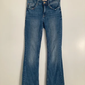 Blå bootcut jeans från Vero Moda - Snygga blå jeans från Vero Moda med bootcut passform och låg midja. Jeansen har klassisk femficksdesign, dragkedja och knapp framtill. Tillverkade i stretchig denim som sitter skönt och formar sig efter kroppen💞