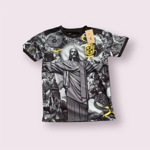 Nike Brasil svartvit fotbollströja - Unik svartvit Brasilien-fotbollströja från Nike med konstnärligt tryck av Kristusstatyn och Rio-motiv på framsidan. Gula detaljer som Nike-logga och Brasil-märke. Kortärmad modell i lätt och ventilerande material, perfekt för match eller träning.