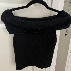 Svart ribbad offshoulder topp Stradivarius - Säljer en svart ribbstickad offshoulder topp från Stradivarius. Toppen har en bred, vikt krage som ger en snygg och trendig look. Perfekt att styla med jeans eller kjol för en cool vibe.