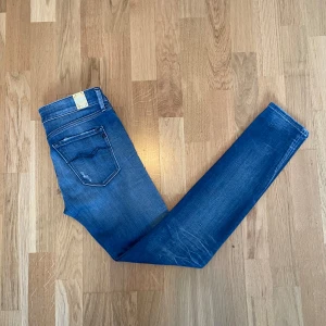 Blå skinny jeans från Replay - Snygga blå skinny dam jeans från Replay med klassisk femficksdesign och diskreta slitningar. Jeansen har normal midja och är tillverkade i stretchigt denim för en bekväm passform. Perfekta till sneakers eller boots för en avslappnad look.