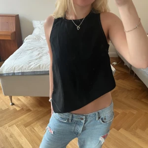 Svart ärmlös linnetopp - Säljer en svart ärmlös linnetopp med rak passform och diskreta sömdetaljer längs kanterna. 