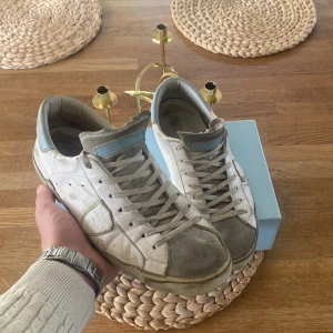 Philippe Model vita sneakers med blå detalj - Snygga vita sneakers från Philippe Model med grå mockadetaljer och ljusblå inslag på häl och plös. Skorna har snörning, rund tå och platt. Fråga på om mer bilder har andvänt skorna i vintras pris kan diskuteras 