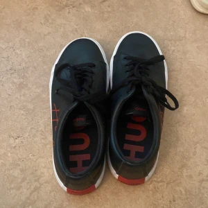 Svarta sneakers från Hugo med röd logga HELT NYA  - HELT NYA Svarta sneakers från Hugo med vit sula och röda detaljer. använt 2 gånger bara och inte kommet till användning
