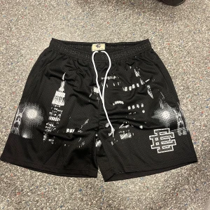 Svarta meshshorts från Eric Emanuel  - Svarta meshshorts från Eric Emanuel med vit snörning i midjan och coolt stadsmotiv i vitt och grått framtill. Shortsen har elastisk midja och är perfekta för en sportig streetwear-look. EE-loggan är tryckt på ena benet. Grymma för sommaren eller träning!