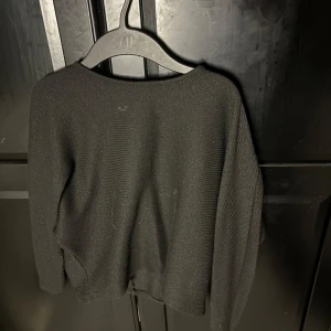 Svart stickad tröja från Gina - En svart stickad tröja från Gina med långärmad design och enkel, stilren look. Tröjan har en rund halsringning och är tillverkad i ett mjukt material som passar perfekt för kyligare dagar.