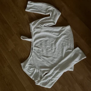 Vit croppad oneshoulder topp - Säljer en vit ribbad croppad topp med lång ärm och en axelbandsdetalj. Toppen har en snygg asymmetrisk oneshoulder-design som ger en cool och trendig look. Perfekt att styla med höga jeans eller kjol.