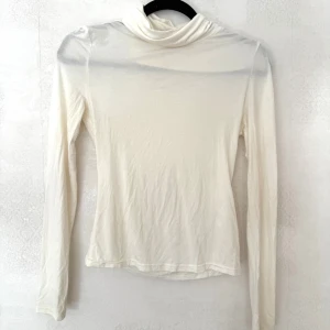 Vit polotröja, storlek S - Tunn och mjuk vit polotröja i storlek S. Tröjan har lång ärm och en hög krage som ger en clean look. Materialet är lätt och stretchigt, perfekt att styla lager på lager. Enkel och stilren design som funkar till många outfits.