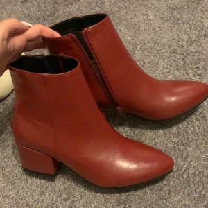Röda boots med klack från Dinsko - Snygga röda boots från Dinsko i storlek 37. Skorna har spetsig tå, låg klack och dragkedja på sidan. Tillverkade i slätt syntetmaterial med en stilren look som passar perfekt till höstens outfits.