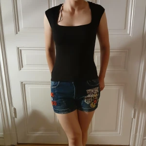 Mickey Mouse jeansshorts med tryck - Unika blå jeansshorts med coola Mickey Mouse-tryck och broderade detaljer i rött och gult. Shorts med låg midja, klassiska fickor och dekorativa nitar. Perfekta för dig som vill sticka ut med en lekfull och retro vibe i sommar. Köpta på en second hand förra året men har bara använt 2 gånger personligen, snygga och i bra kvalitet och av det jag kan se ser jag inte att några rihnestones saknas. Midjemåttet rakt över är:36cm men är väldigt strechigt tyg, jag på bilden är ca.160cm lång, midwaist❤️