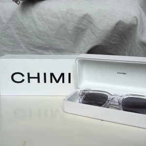 Chimi transparenta solglasögon - Snygga solglasögon från Chimi med transparent båge och mörkgrå tonade glas. Rektangulär form som ger en modern vibe. Kommer i originaletui och box. Perfekta för dig som vill sticka ut med stilrena accessoarer. Köpta 2024, använda ett fåtal gånger 