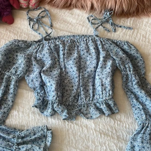 Blommig blå blus med volang - Supersöt blommig off shoulder blus i ljusblått med volangkant och långa puffärmar. 