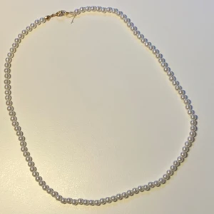 Klassiskt pärlhalsband med guldlås *Endast 1 Kvar* - Stilrent halsband med vita pärlor i rund form och ett snyggt guldfärgat lås. Perfekt för dig som vill ha en tidlös och elegant accessoar som lyfter vilken outfit som helst. Pärlorna är jämnt placerade och halsbandet har en enkel men lyxig känsla.