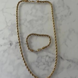 Guldfärgat halsband och armband set - Säljer ett snyggt set med guldfärgat halsband och matchande armband. Båda har tvinnad kedja som ger en cool och trendig look. Perfekt för dig som gillar klassiska smycken med lite extra edge. Finns 2 såna om ni skulle vilja ha fler 