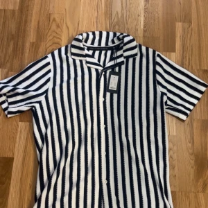 Randig kortärmad skjorta från lager 157 - Snygg kortärmad skjorta från lager 157 med svartvita vertikala ränder och klassisk krage. Skjortan har knäppning framtill och är perfekt för en stilren look. Materialet känns mjukt och svalt, perfekt för varmare dagar. Säljer då det inte var min still 