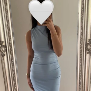 Ljusblå långklänning i stretch - Supersnygg ljusblå långklänning i figurnära modell med hög hals och ärmlös design. Klänningen är tillverkad i ett stretchigt material som sitter tight och framhäver siluetten. Endast använt en gång 