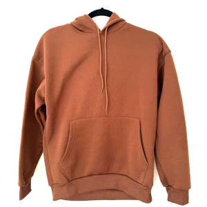 Brun hoodie med huva och ficka - Snygg brun hoodie i storlek S med klassisk känguruficka framtill och dragsko i huvan. Tröjan har ribbade muddar vid ärmslut och nederkant, samt en avslappnad passform. 