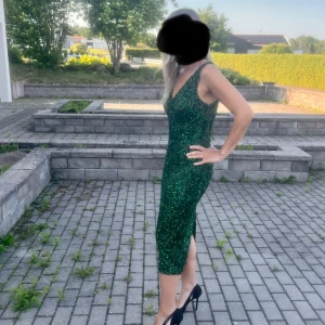 Grön glittrig klänning med snörning - Supersnygg grön glittrig klänning med v-ringning och smickrande passform. Klänningen har snörning i ryggen, slits bak och är ärmlös. Perfekt för dig som vill sticka ut på festen! Klänningen är använd endast ett par timmar.
