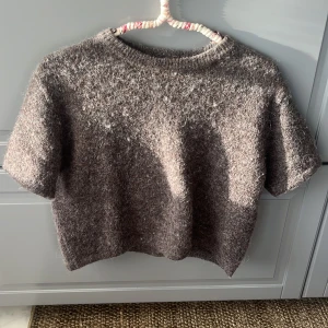 Brun stickad tröja från Gina Tricot - Mysig brun stickad tröja från Gina Tricot med korta ärmar och rund hals. Tröjan har en fluffig och lite luddig yta som ger en cool och avslappnad vibe. Perfekt att styla med jeans eller kjol för en chill look. Privat för bild på!😝