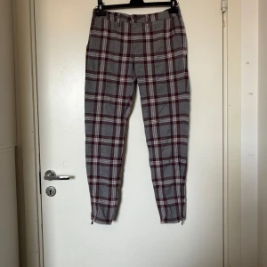 Rutig byxa från Odd Molly, grå & vinröd - Snygga byxor i grått med vinröda och vita rutor. Modellen är slim och har dragkedjor vid bensluten. Perfekta för dig som gillar en trendig och bekväm look. Gjorda i mjukt bomullstyg. Från märket Odd Molly i storlek 1 som ungefär motsvarar en storlek S. Fint skick, men kan ha lite ytludd. Mer använda. 