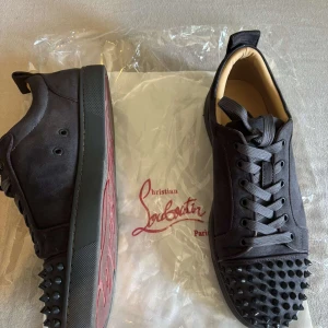 Christian Louboutin gråa sneakers med nitar - Gråa sneakers från Christian Louboutin i mocka med ikoniska röda sulor och gra nitar på tån. Skorna är nästan helt nya använda 2 gånger bara(priset går att diskutera)